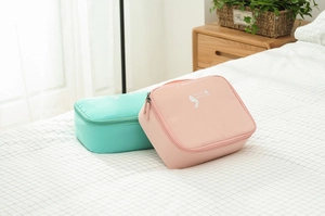 Pink and green travel toiletry bags with top handles and zippers on a cozy bed