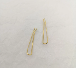 Macro shot of two golden U-shaped hair pins on textured white paper backdrop