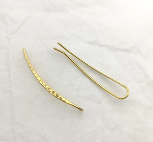 Macro detail of gold U-shaped earring featuring a modern hammered metal surface texture