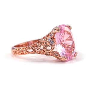 Detail of rose gold filigree ring featuring an oval pink gemstone and white side stones