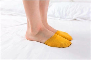 Detail of ginger yellow cotton no-show socks with non-slip cuff on model's feet