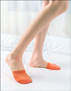 Detailed close-up of orange cotton invisible half-palm socks worn by a model on white bed
