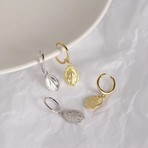 Macro shot of silver and gold religious coin drop earrings on a white aesthetic background