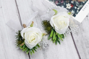 Dettaglio di boutonnière con rose bianche artificiali, foglie verdi e perle su legno