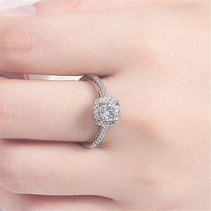 Close-up of a square halo diamond ring with round center stone and pave band on finger
