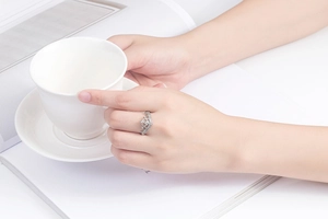Close-up of a silver zircon crown ring on hand holding a white porcelain cup