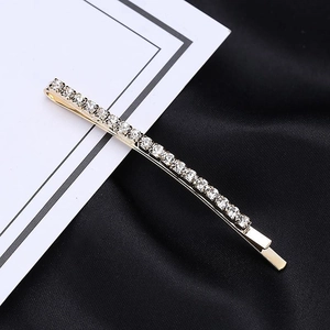 Detail of single gold rhinestone hair clip on white card against black silk background