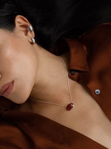 Close-up of minimalist silver ear cuff and matching reddish pendant necklace on a model