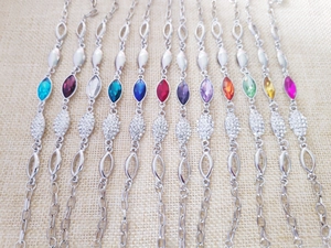Close-up of 12 silver bracelets with colorful oval gemstones and sparkling rhinestones