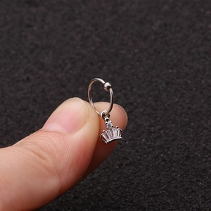 Dettaglio macro di un anello in acciaio argento con ciondolo a corona in zircone tra le dita