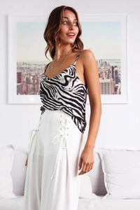 Detail shot of a zebra print camisole paired with white lace-up trousers in a bright studio