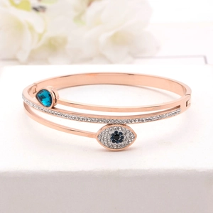Détail d'un bracelet œil porte-bonheur en or rose avec cristaux bleus sur socle blanc