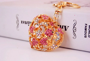 Detailed close-up of golden hollow heart keychain with pink rhinestones on a white book