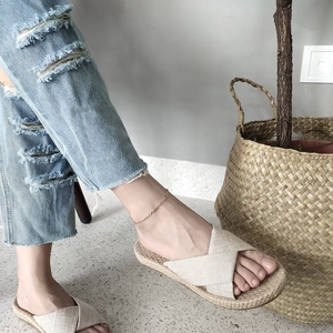Detail of a gold ankle bracelet worn with beige linen cross-strap slides on model