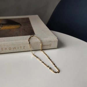 Golden 925 sterling silver anklet with unique flat oval links draped over a book spine