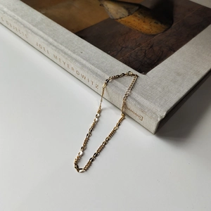 Detailed close-up of a gold-plated flat chain link anklet draped over an art book
