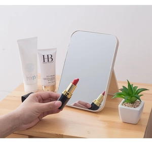 Close-up of portable white folding makeup mirror on wooden desk with sharp reflection