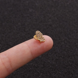 Macro shot showing the tiny size of a gold bow piercing stud held against a finger
