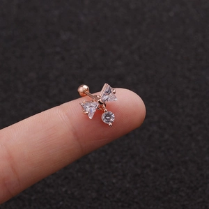 Detailed view of a rose gold bow earring with zircon pendant held on a fingertip