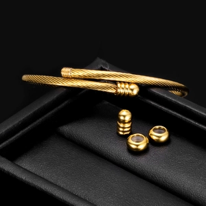 Detail of golden stainless steel cable bangle with three matching beads on a black gift box