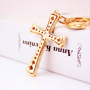Elegant gold cross keychain with floral crystal inlay on an open vintage book background