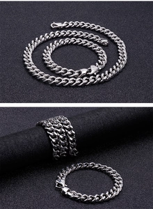Silver stainless steel Cuban link necklace, bracelet, and ring set on matte black surface