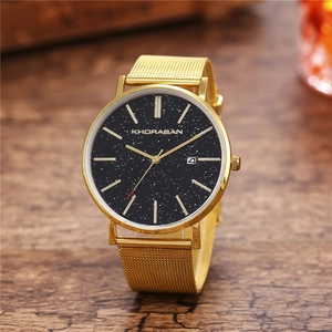 Detail of men's gold mesh watch with black starry dial and date window on wooden table