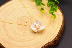 Detail of baroque pearl flower pendant with pink center on gold necklace and wood background