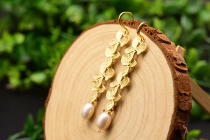 Macro view of gold flower petal long drop earrings with elegant natural pearls