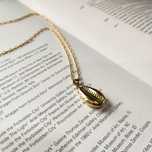 Detailed view of a golden shell pendant necklace lying on an open vintage art book