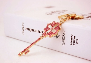 Detailed close-up of golden four-leaf clover key pendant with pink rhinestones on a book