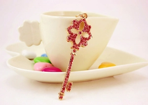 Detail of a golden key pendant with pink rhinestones leaning on a heart-shaped cup