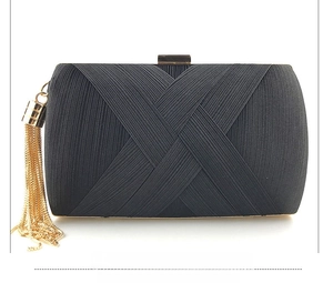 Detail of black pleated fabric clutch bag with elegant golden tassel and metal clasp