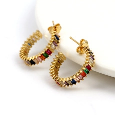 Close-up of gold C-shaped earrings set with colorful zircon on a white plate rim