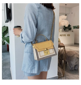 Close-up of yellow and beige patchwork handbag with gold chain strap in a cafe setting
