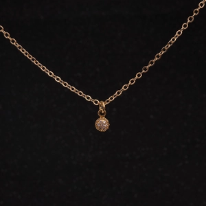 Close-up of a gold necklace with a sparkling cubic zirconia floral pendant on black background