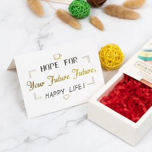 Minimalist white gift box with red raffia filling and gold foil greeting card on marble