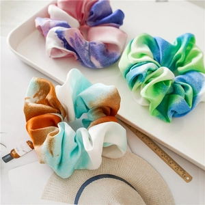 Detail showing three tie-dye gradient scrunchies in pastel colors on a white tray