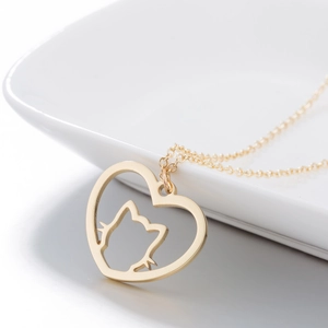 Golden stainless steel heart pendant necklace with cat silhouette on white ceramic plate