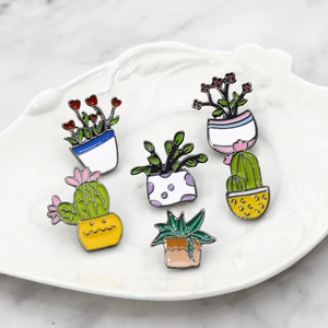 Set of five colorful cartoon enamel cactus plant pins on a white leaf-shaped ceramic dish
