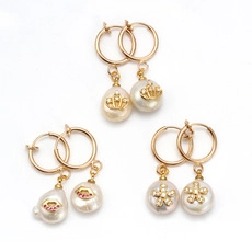 Detailed view of gold earrings with crown, red lips, and flower motifs on pearls