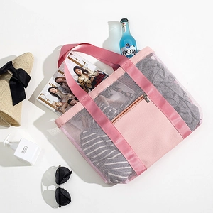 Pink mesh beach tote bag with front zipper pocket and vacation accessories on white background