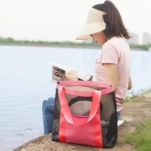 Large black mesh beach bag with pink straps shown in a scenic outdoor lakeside setting