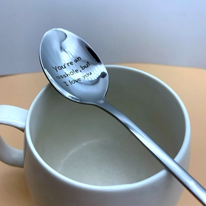 Macro detail of custom engraved stainless steel coffee spoon on white ceramic cup