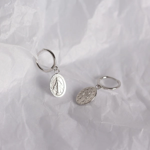 Macro detail of S925 sterling silver Virgin Mary coin drop earrings on textured white paper