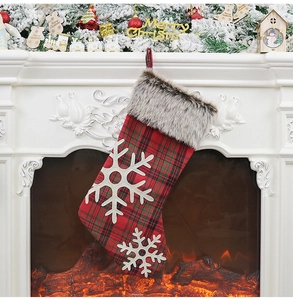 Detail of a red and green plaid Christmas stocking with white snowflake decor on a fireplace
