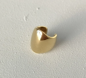 Close-up of a minimalist golden polished ear cuff or ring on white textured background