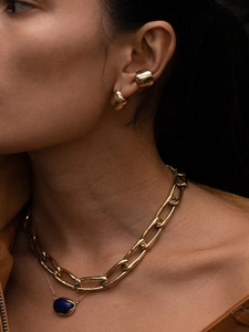 Detail shot of chunky gold clip-on earrings and layered blue pendant necklaces on a model