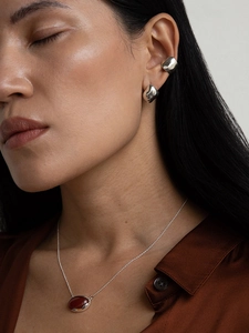 Close-up of silver irregular earrings and necklace with a reddish brown gemstone pendant