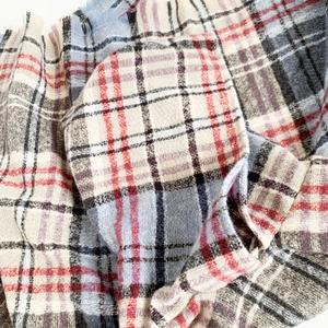 Dettaglio del tessuto poncho a quadri rosso e blu con texture morbida e frange